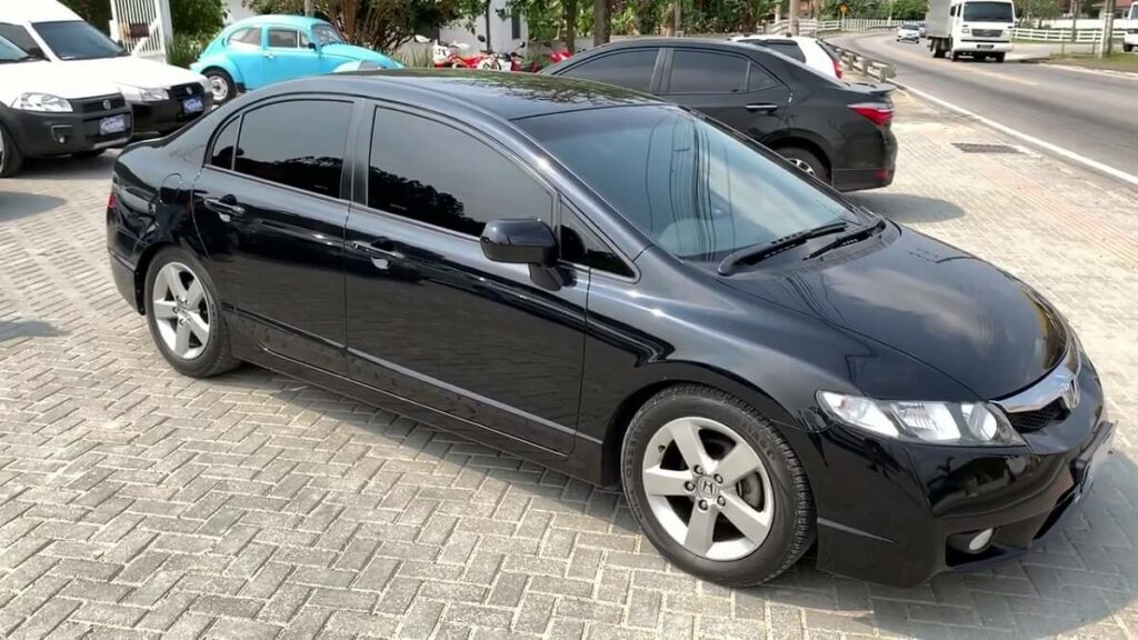 Foto lateral de um Civic 2009 preto fechado na película estacionado na praça de uma cidade 