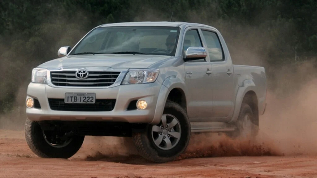Foto frontal de uma Hilux 2015 prata andando na terra