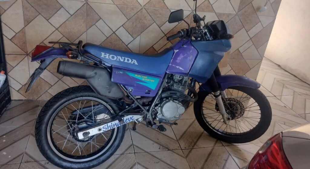 Honda NX 200 1995 roxa parado na parede.