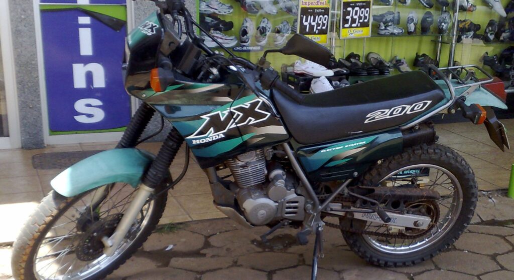 Honda NX 200 2001 verde parado na diagonal.