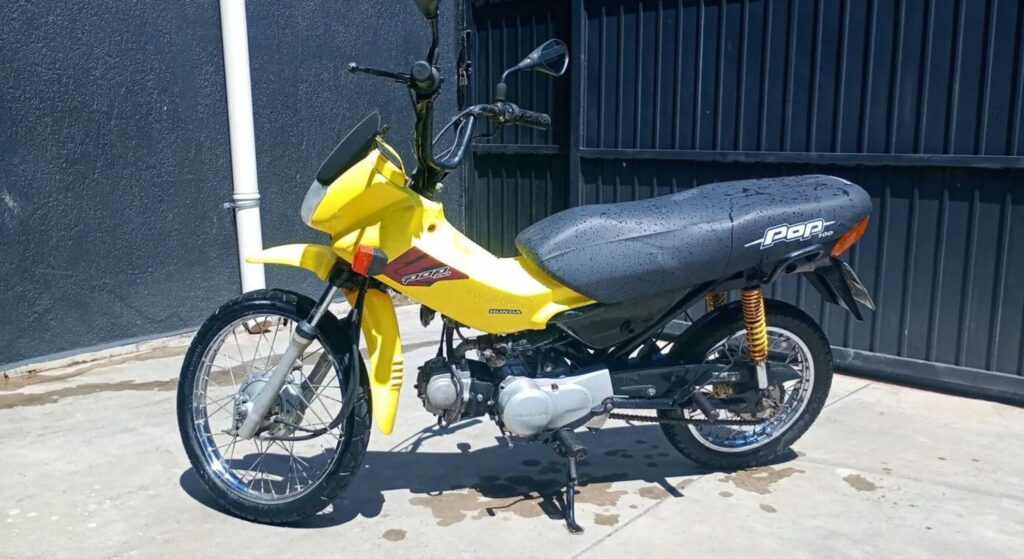 Honda Pop 2007 amarela parado de lado.