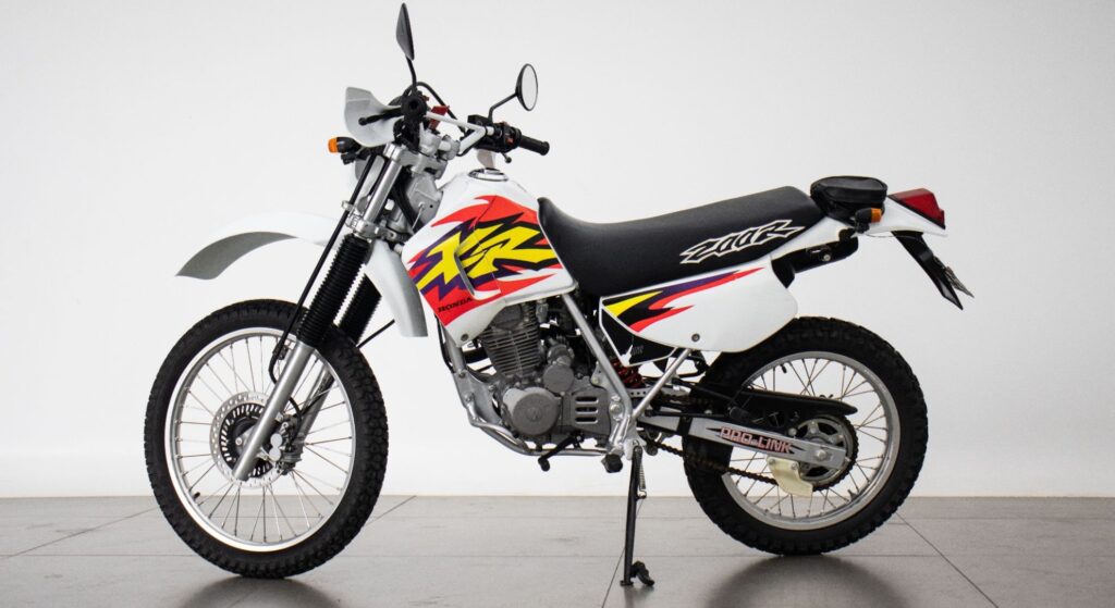 Honda XR 200 R 1999 branco com vermelho parado de lado.
