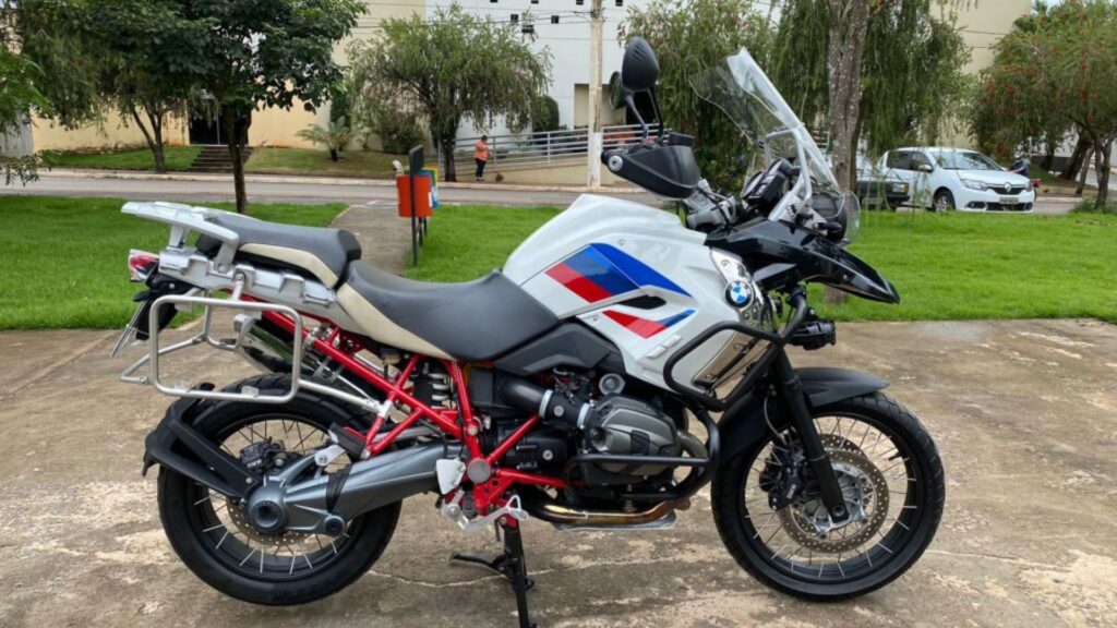 Lateral da BMW R 1200 GS 2012 branca com detalhes em azul e vermelho parada em uma praça.