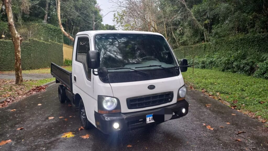Kia Motors Bongo 2002 branco parado na diagonal no meio da estrada com os faróis acesos.