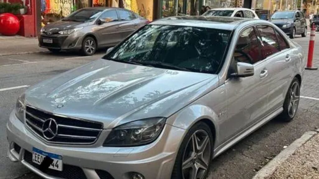 Mercedes-Benz C-63 2009 prata na diagonal em um estacionamento na beirada da estrada.