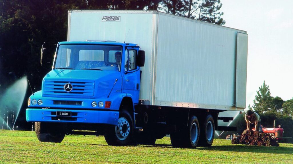 MERCEDES-BENZ L-1620 2001 azul com baú parado na diagonal em cima de um gramado.