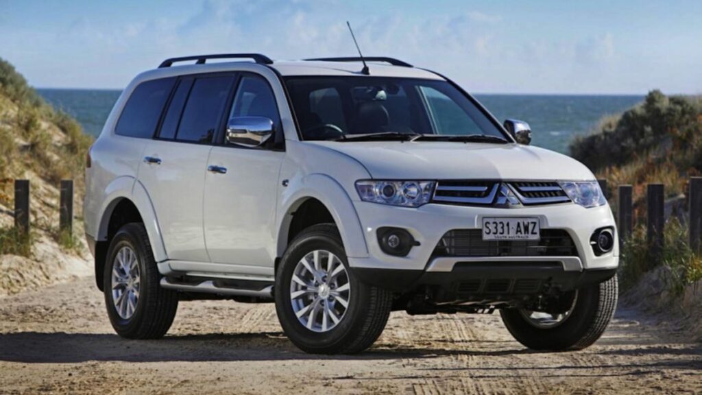 Mitsubishi Pajero 2014 branca na diagonal em um estrada de areia próximo do mar.