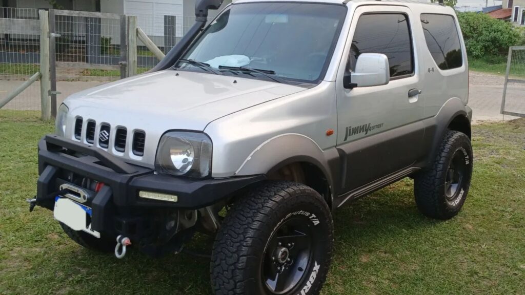Suzuki Jimny 2003 prata parado em um gramado na diagonal.