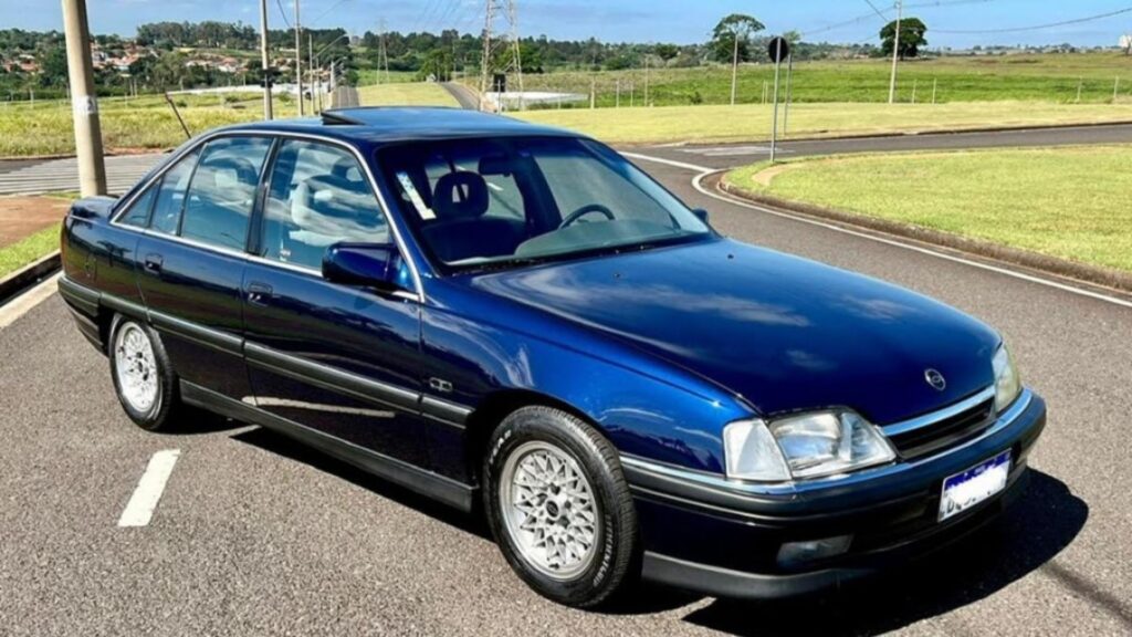 Chevrolet Omega 1993 azul parado na diagonal no meio da estrada.