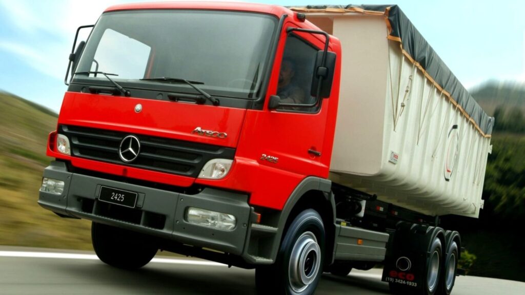 MERCEDES-BENZ Atego 2005 vermelho em movimento na estrada com uma caçamba e com uma lona preta.