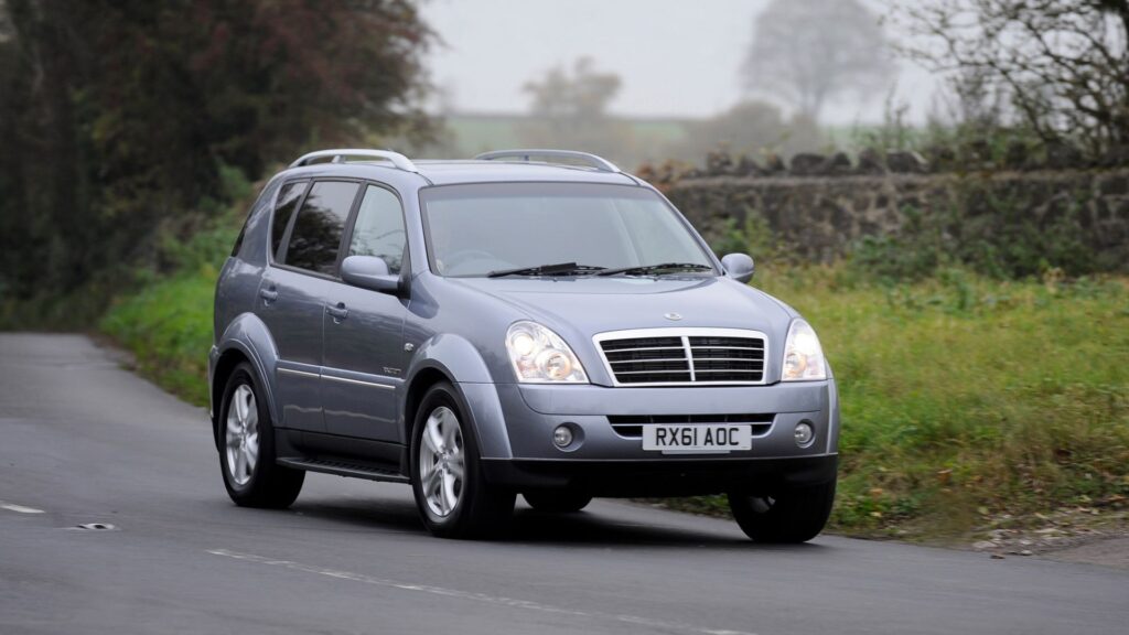 SSANGYONG Rexton 2012 cinza parado na diagonal em uma estrada com neblina no fundo.