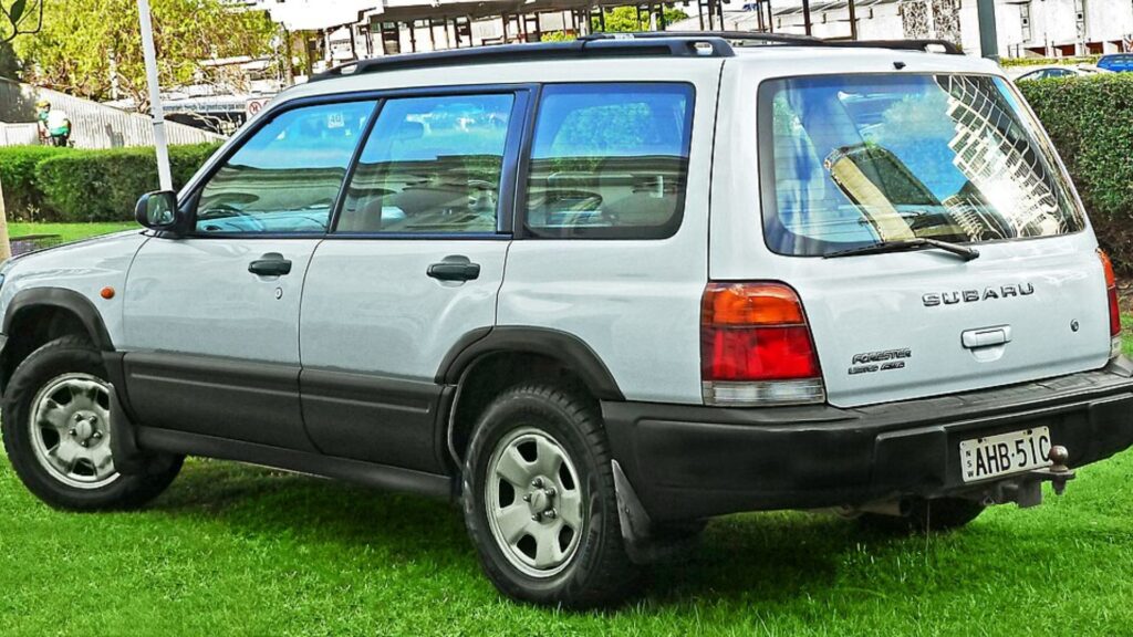 Traseira do Subaru Forester 1999 prata parado na diagonal em cima de um gramado.