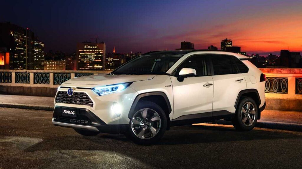 Toyota RAV4 2020 branco parado na diagonal com os faróis acesos.