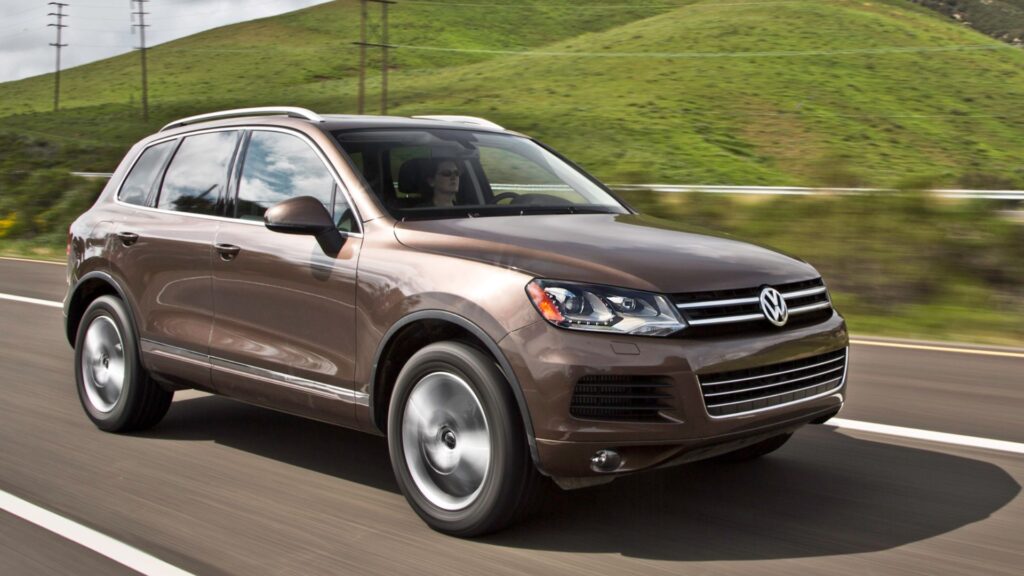 VolksWagen TOUAREG 2013 marrom em movimento na estrada com um gramado no fundo.