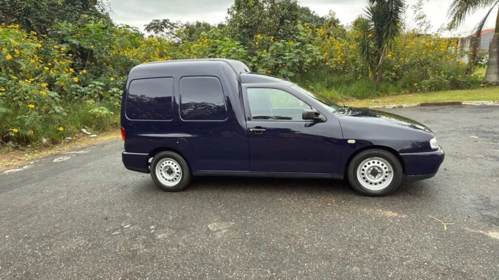 Lateral da VolksWagen Van 1999 azul parada.