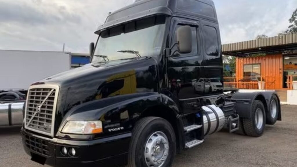 VOLVO NH-12 2004 preto parado em uma loja que revende caminhões na diagonal.