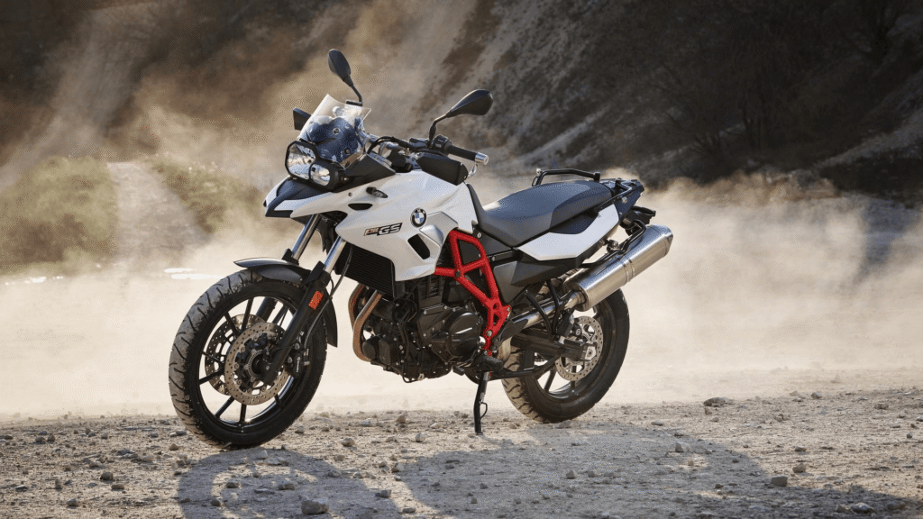 BMW F 700 2018 branca parada na diagonal em meio de uma poeira de areia.