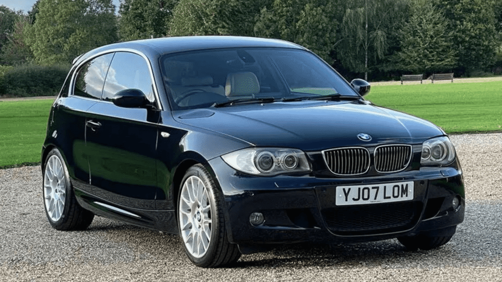 BMW 130i 2007 preto parado na diagonal com um gramado no fundo.