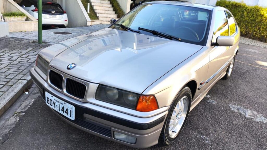 BMW 318i 1995 cinza parado na diagonal.