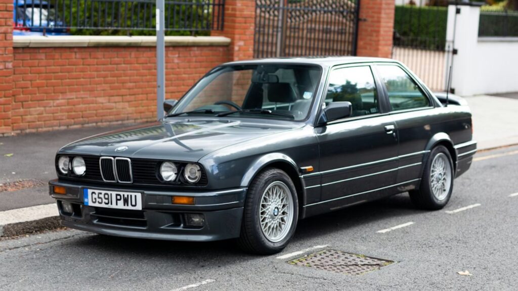 BMW 325i 1990 cinza parado na diagonal.
